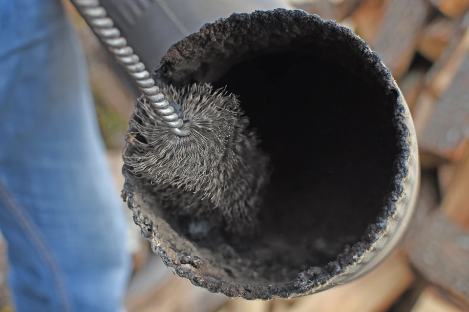 Scène d'intérieur d'atelier où une brosse métallique circulaire est insérée dans un conduit ou tuyau noirci par la suie