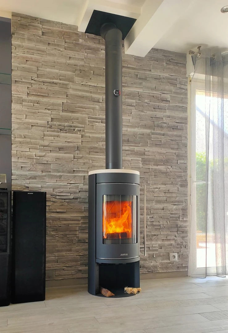Intérieur contemporain, poêle à bois design cylindrique en acier laqué anthracite, vitre panoramique bombée avec feu actif visible, bûches en combustion